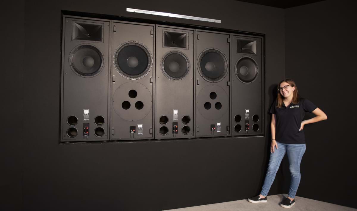 A women standing next to massive speakers that are use in home theater rooms